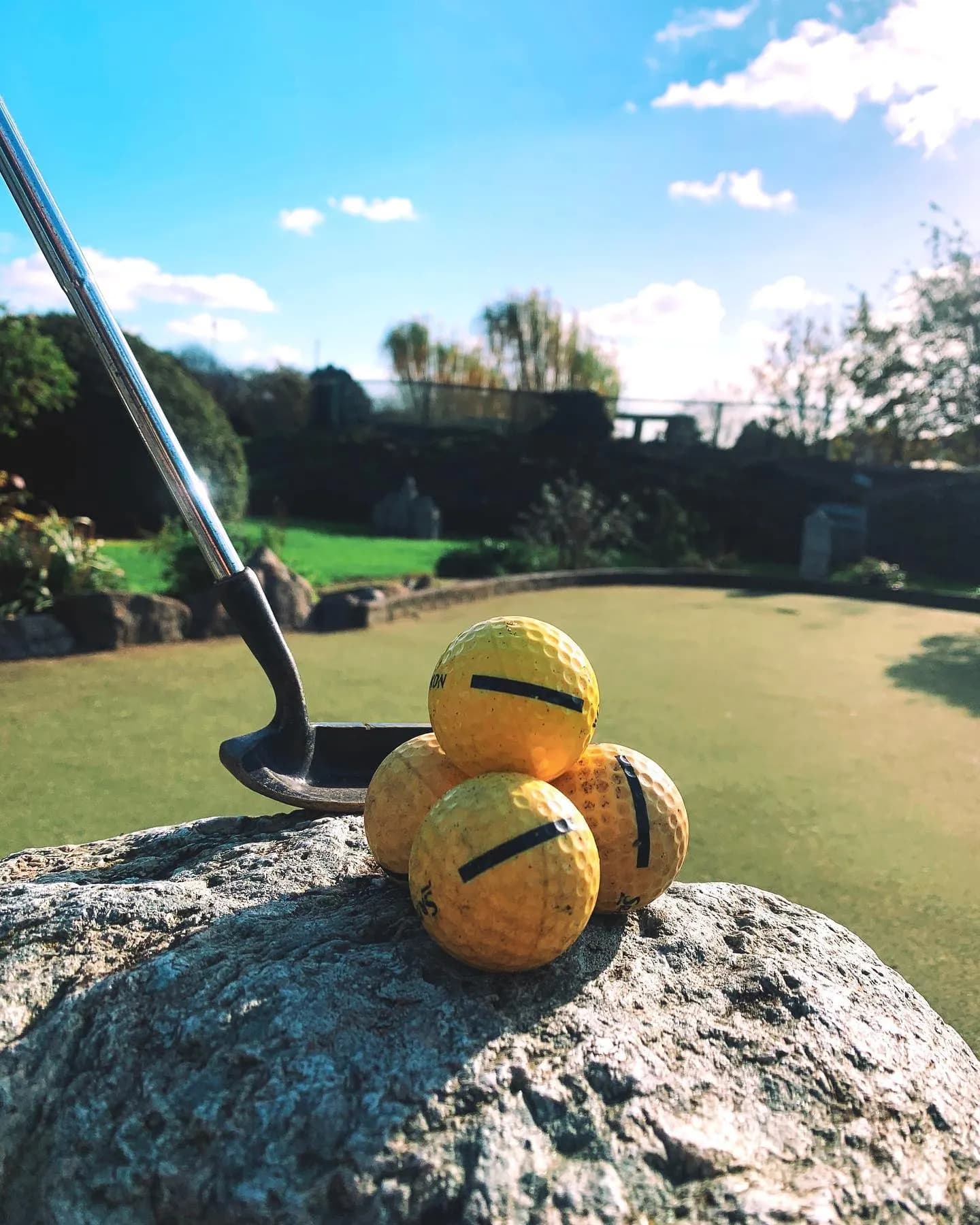 Gele golfballen op een rots naast een putter
